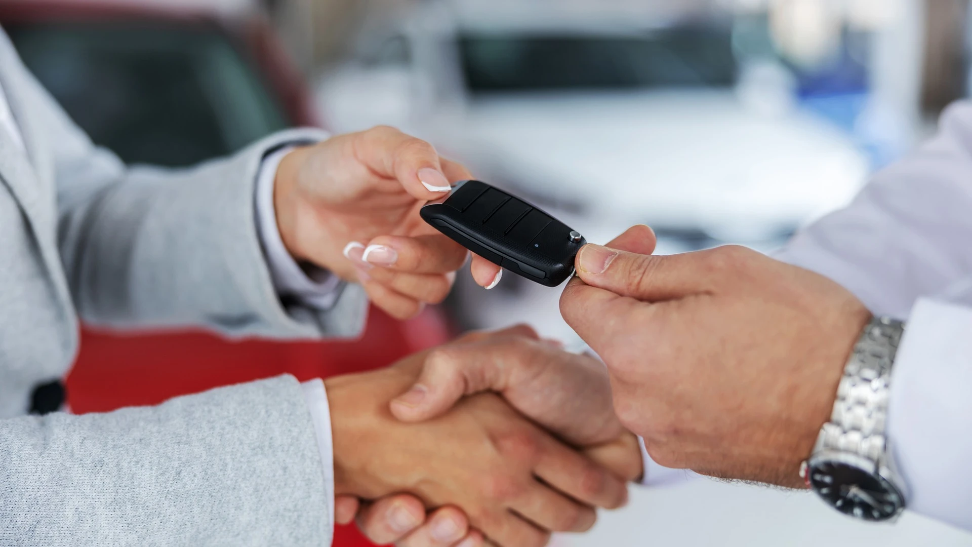 Closeup of car seller and a buyer shaking hands while standing in car salon. Seller handing car keys to a buyer.