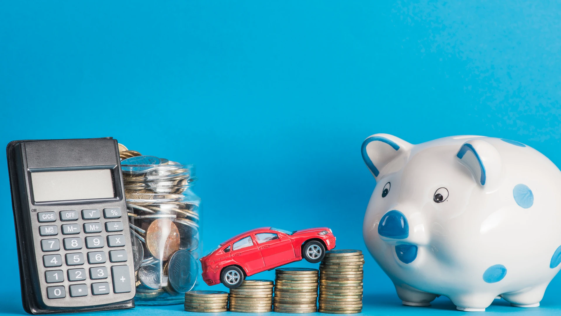 Car over the coin stack with calculator; glass jar; ceramics piggybank against blue background