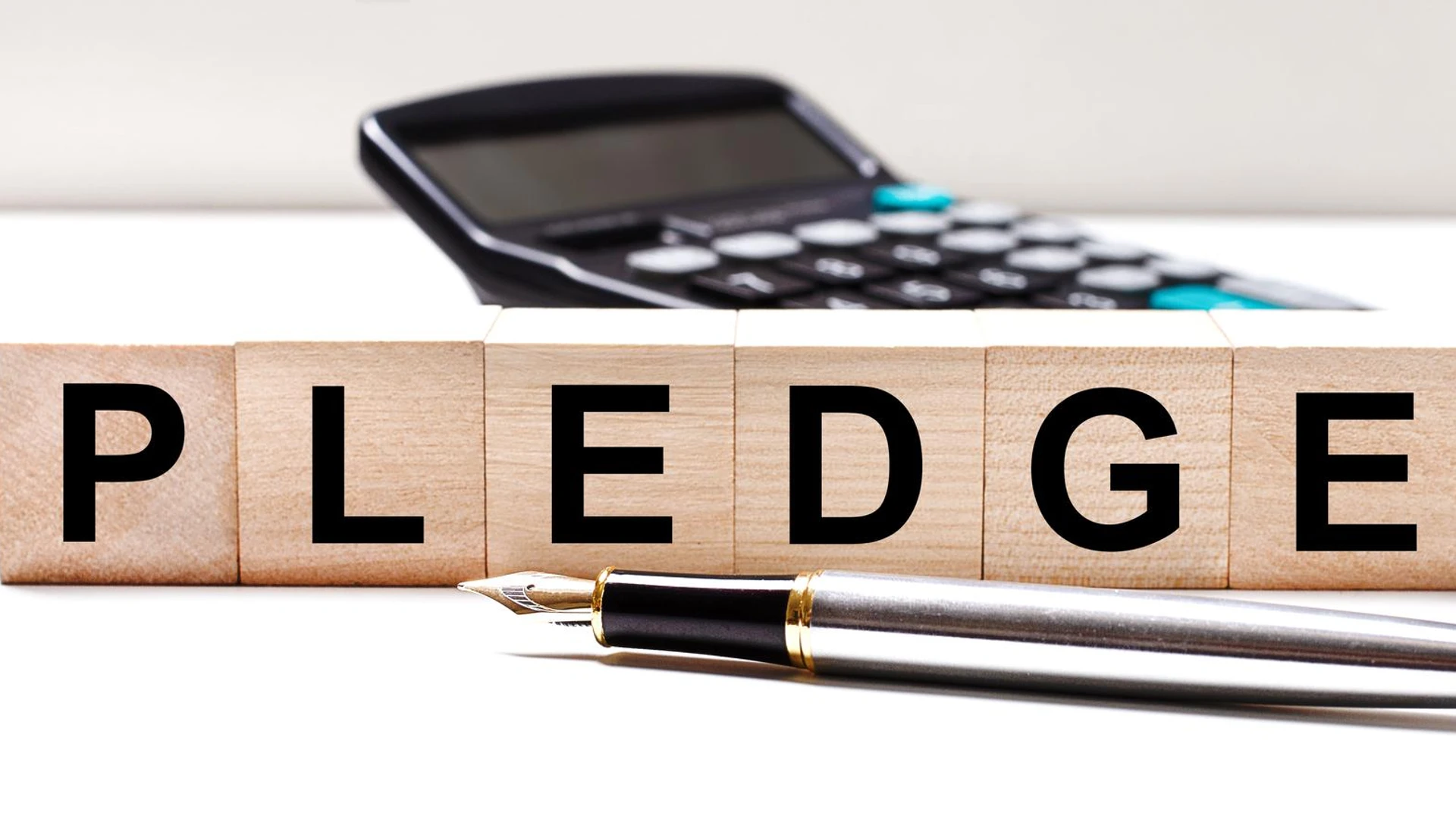 The light table has a black calculator a fountain pen and wooden cubes with the text PLEDGE Business concept