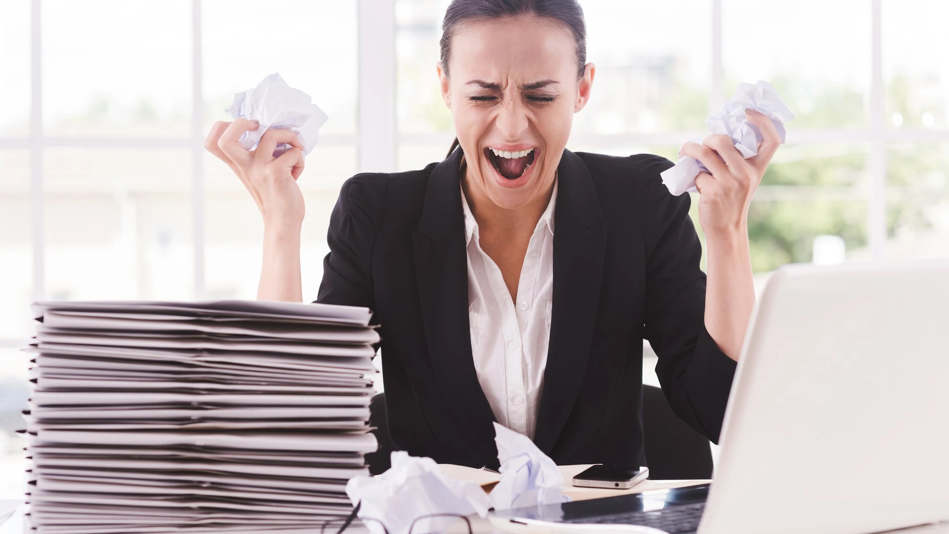 That is too much for me! Furious young woman in formalwear holding papers in hands and shouting while sitting at her working