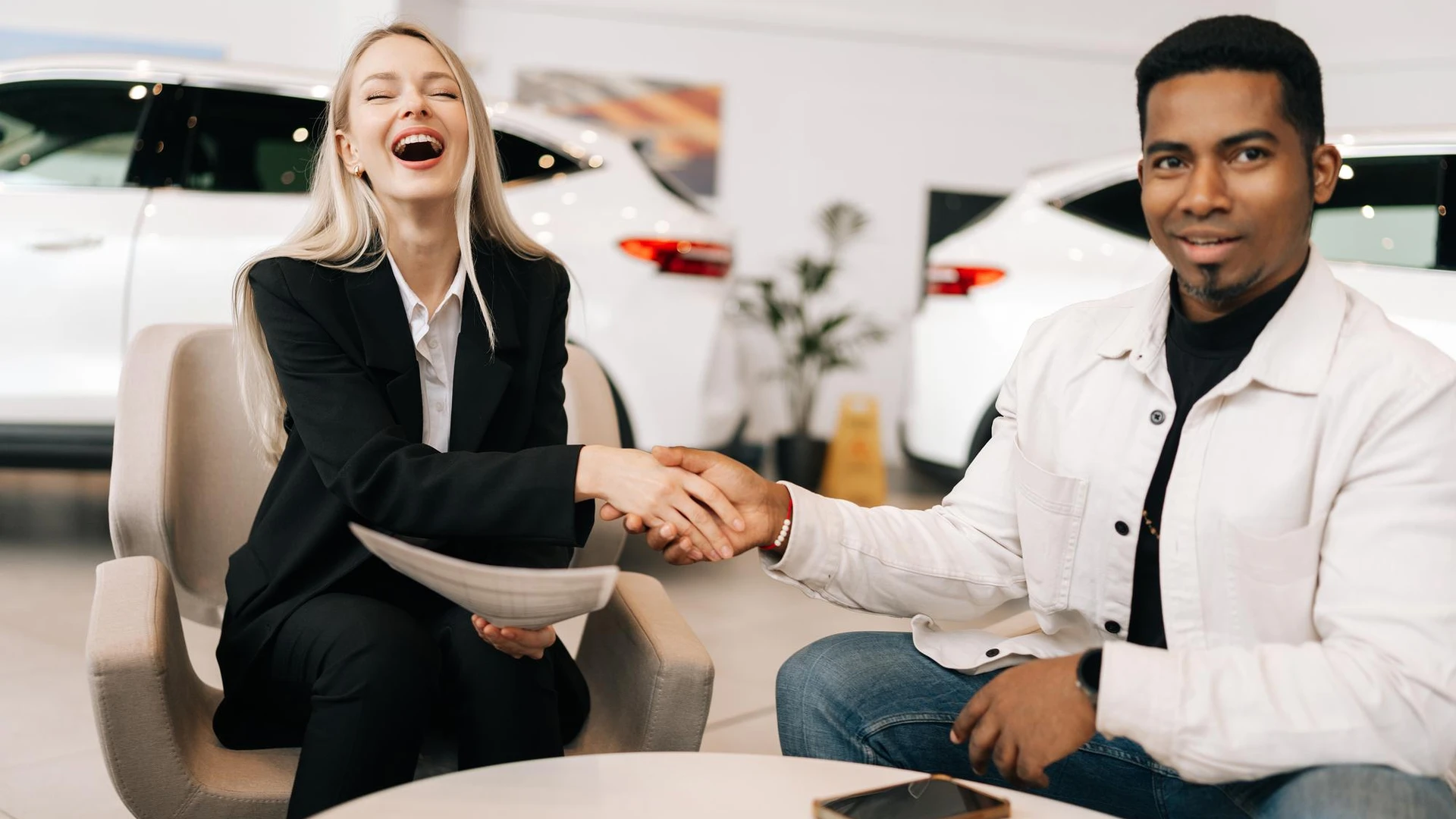 Happy black customer getting approved car purchase agreement in dealership laughing female car
